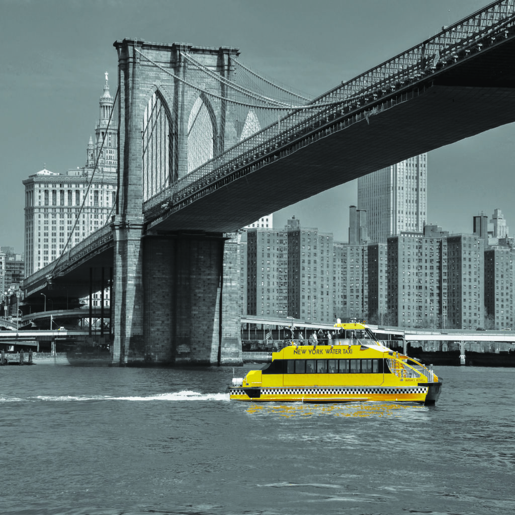 A yellow New York water taxi under a bridge